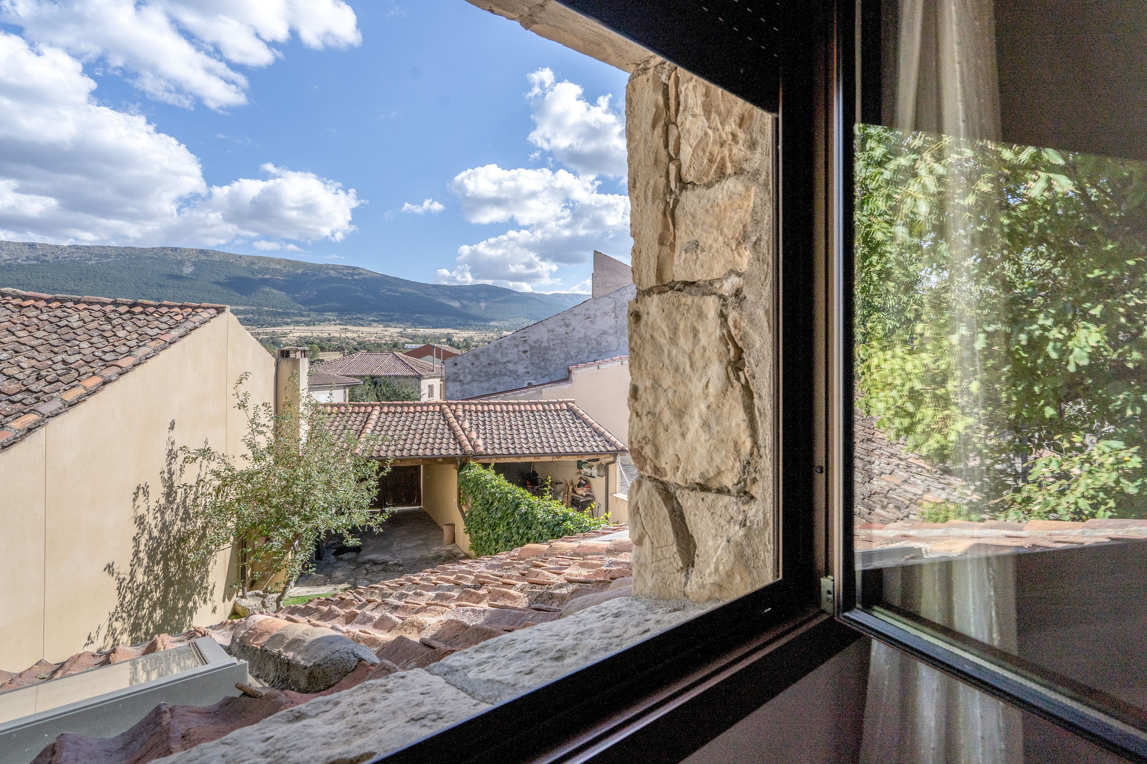 Vista desde una ventana que da a un patio con arquitectura tradicional, incluyendo tejados de teja y muros de piedra.