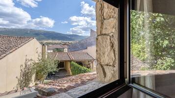 Vista desde una ventana que da a un patio con arquitectura tradicional, incluyendo tejados de teja y muros de piedra.