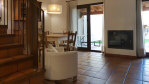 A spacious living area with a staircase, a dining table, chairs, a sofa, a TV, and a fireplace. - Country House 'Fuentebuena' with Mountain View, Private Terrace and Wi-Fi (Matabuena)