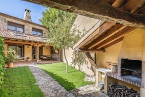 Un patio con un sendero de piedra, una pérgola de madera, una zona de barbacoa y un edificio de piedra con techo de tejas.