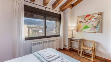 Une chambre à coucher avec un lit, un radiateur, une fenêtre avec des rideaux, un bureau, une chaise et un tableau accroché au mur.