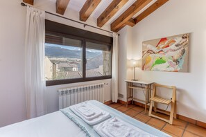 A bedroom with a bed, a radiator, a window with curtains, a desk, a chair, and a painting on the wall. - Country House 'Fuentebuena' with Mountain View, Private Terrace and Wi-Fi (Matabuena)