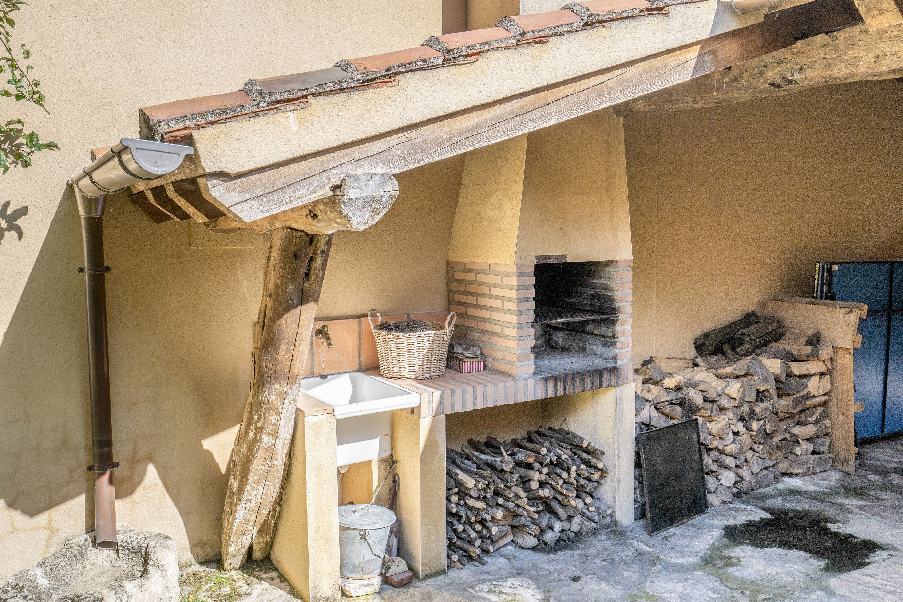 Una cocina rústica al aire libre con un horno de ladrillo, un lavamanos y un banco de madera.