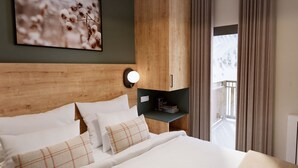 Hotelkamer met een houten hoofdeinde, een bed met witte lakens, een nachtkastje met een lamp en zicht op een besneeerd landschap door het raam.