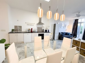 Une cuisine moderne avec des meubles blancs, un coin repas avec des chaises blanches et un salon avec un canapé bleu.