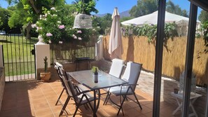 Une terrasse extérieure avec une table en verre, des chaises blanches, un cactus et une bouteille de vin.