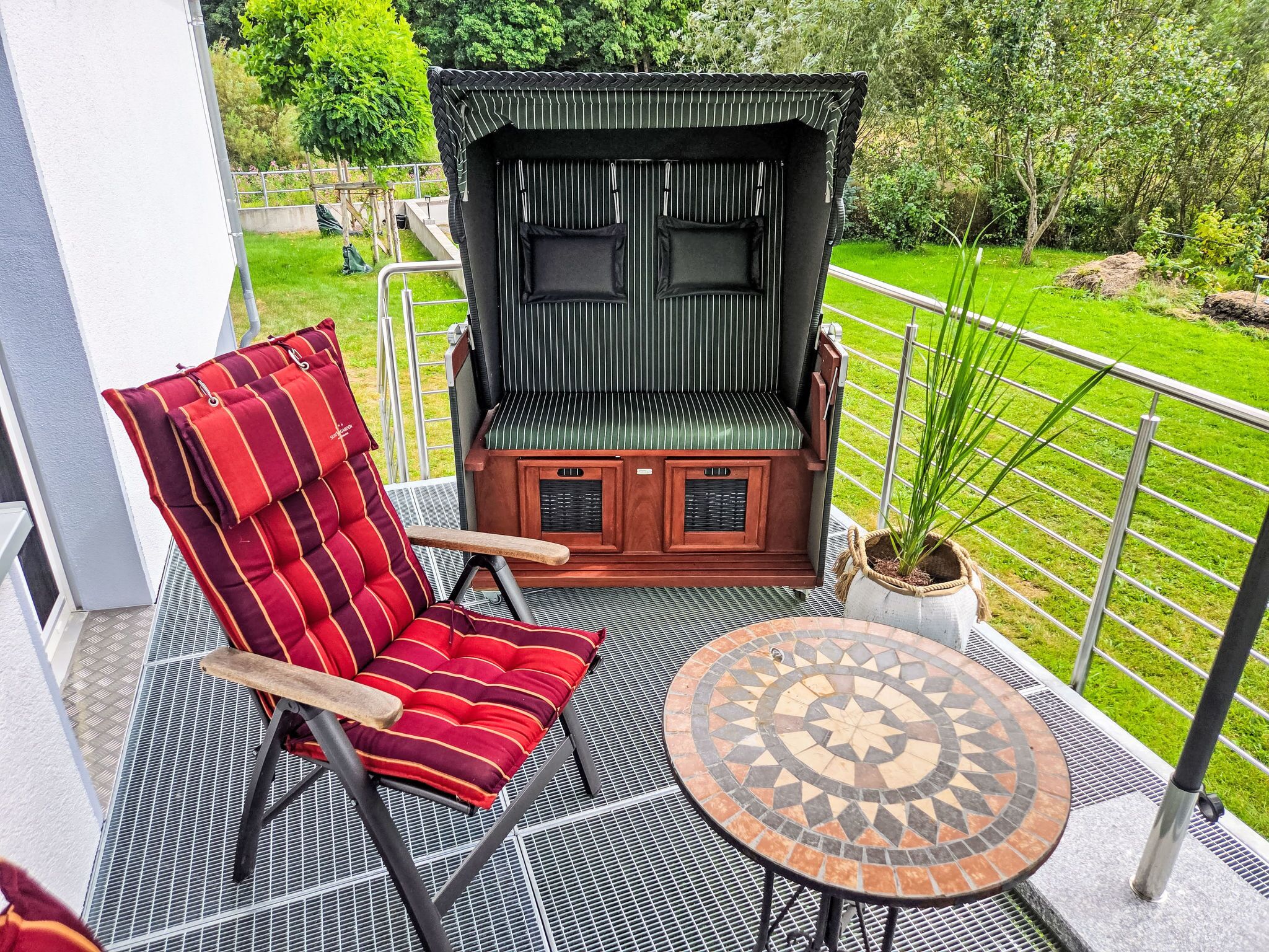 A balcony with a red-striped chair, a small table, and a wooden bench with a green cushion.