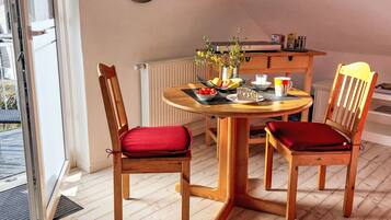 Ein Essbereich mit einem runden Holztisch, zwei Holzsesseln mit roten Kissen, einer kleinen Topfpflanze und einer Uhr an der Wand.
