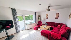 Un soggiorno con un divano rosso, un tavolino in legno, una TV e una ventola a soffitto.