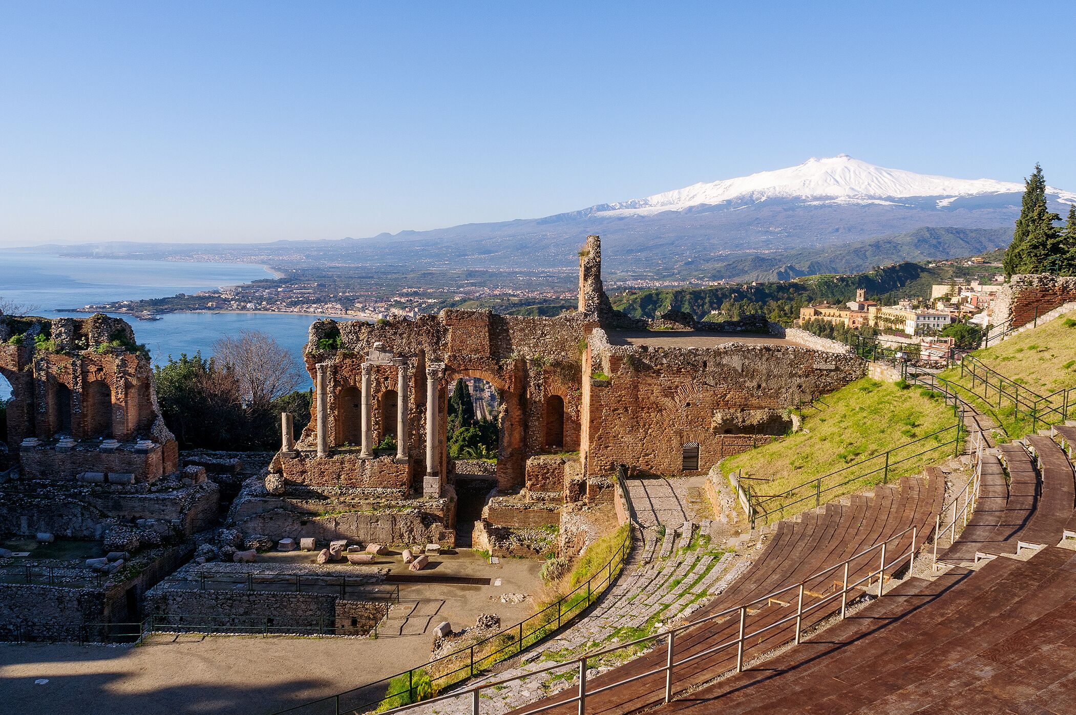 Ancient ruins with a view of a snow-capped mountain and a body of water in the distance.