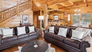 L’intérieur d’un chalet confortable, avec deux canapés en cuir, une table à manger, un coin cuisine et un escalier.