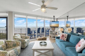 Un balcón amplio con vistas al océano, amueblado con sillas azules y una mesa blanca.