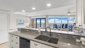 A modern kitchen with a large island, a double sink, and a view of the ocean through large windows. - Sea Gull #503L: Beachfront 2 Bedroom 2 Bathroom With Spectacular Views and 24 Hour Management (Port Aransas)