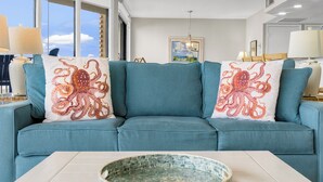 A teal sofa with octopus-themed pillows, a round mosaic tray, and a view of the ocean through large windows. - Sea Gull #503L: Beachfront 2 Bedroom 2 Bathroom With Spectacular Views and 24 Hour Management (Port Aransas)