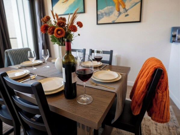 Una mesa de comedor dispuesta con platos, vasos, una botella de vino y un florero con flores.