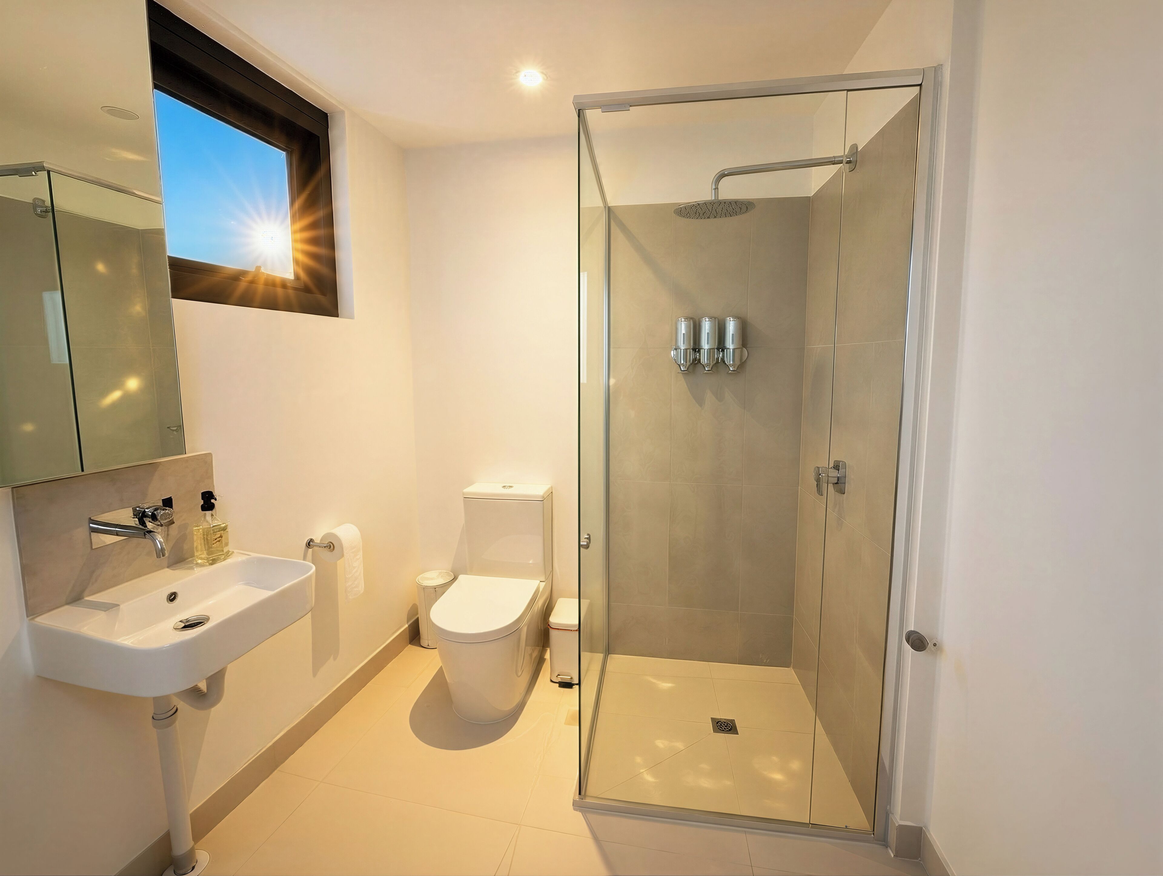 Uma casa de banho moderna com chuveiro em cabine de vidro, sanita e lavatório com espelho.