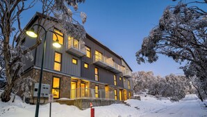 Un edificio de varios pisos con balcones, fachada de piedra y un paisaje cubierto de nieve.