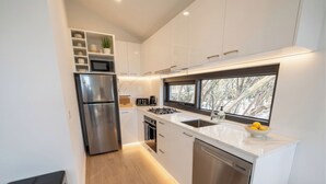 Una cocina moderna con armarios blancos, electrodomésticos de acero inoxidable, horno empotrado y ventana con vistas a árboles.