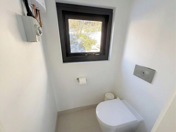 A small bathroom with a toilet, a window, and a wall-mounted heater.