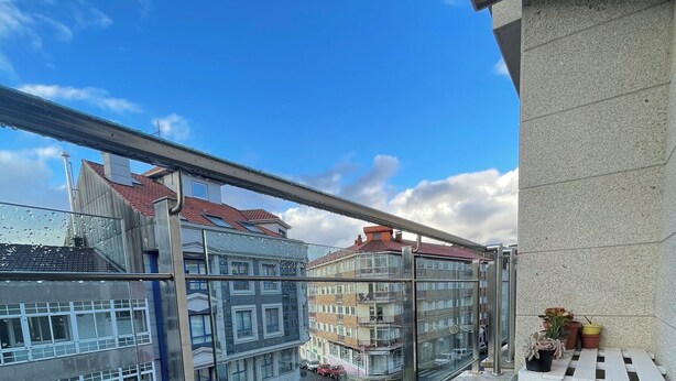 A balcony with a glass railing overlooking a street with buildings.