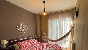 A bedroom with a bed, a nightstand, a lamp, a TV, and a hammock.