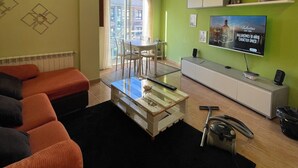 A living room with a sofa, a coffee table, a TV, and a dining area with chairs and a table.
