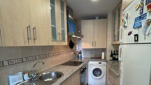 A compact kitchen with wooden cabinets, a stainless steel sink, a built-in washing machine, and a refrigerator.