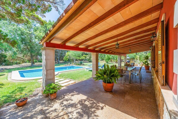A covered patio area with a pool, outdoor furniture, and potted plants.