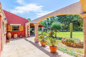 A courtyard with a red building, large terracotta pots, a cactus, and a pool in the background.