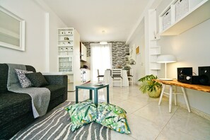 Un salon moderne avec un canapé, une table basse, un coin repas avec des chaises, une cuisine en arrière-plan et une grande fenêtre avec des rideaux.