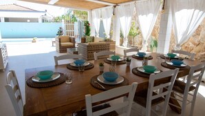 An outdoor dining area with a wooden table set for four, surrounded by white chairs. - Villa 'Casa Giò' with Private Pool, Wi-Fi and Air Conditioning (Santa Maria del Focallo)