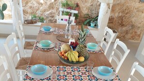 A wooden dining table with a fruit centerpiece, white chairs, and a stone wall backdrop. - Villa 'Casa Giò' with Private Pool, Wi-Fi and Air Conditioning (Santa Maria del Focallo)