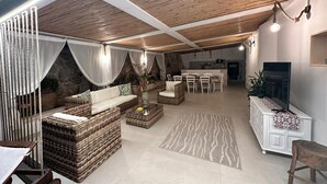 A spacious living area with a high ceiling, wicker furniture, a stone wall, and a television. - Villa 'Casa Giò' with Private Pool, Wi-Fi and Air Conditioning (Santa Maria del Focallo)