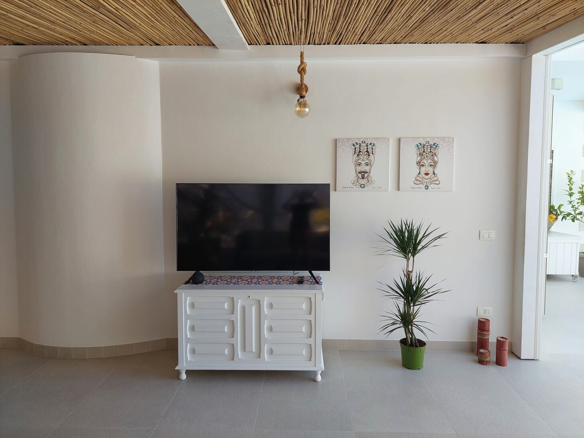 Una sala moderna con una televisión de pantalla plana sobre un mueble blanco, una planta en maceta y una obra de arte en la pared.