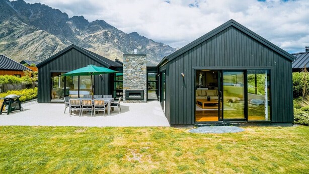 A modern house with a patio, a stone fireplace, and a view of mountains.