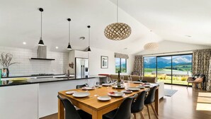 A modern kitchen with a central island, dining area with chairs, and large windows offering a view of the outdoors.