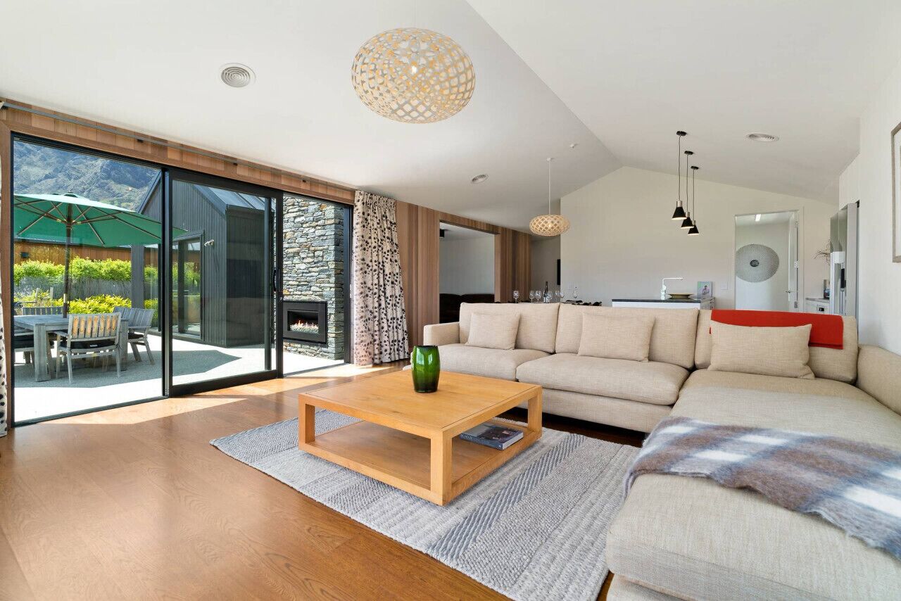 A modern living room with a wooden coffee table, a beige sofa, and a glass sliding door leading to a patio.