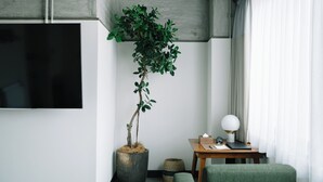 A modern living room with a large potted plant, a flat-screen TV, a wooden side table, and a green armchair.