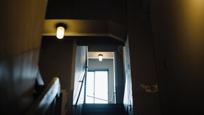 A dimly lit stairwell with a light fixture above the door, leading to a bright room.