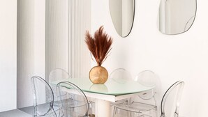 Een eethoek met een glazen tafel, transparante stoelen en een vaas met gedroogde planten.