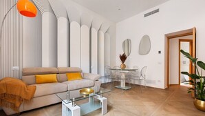 Een moderne woonkamer met een bank, een glazen salontafel en een eetgedeelte met een glazen tafel en stoelen.
