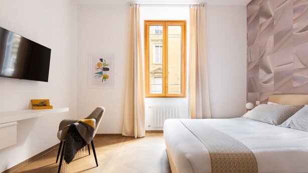Een moderne hotelkamer met een bed, een stoel, een televisie, een raam met gordijnen en een muur met een geometrisch patroon.