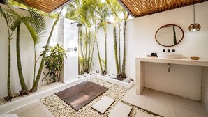 Ein modernes Badezimmer mit Holzboden, einem weißen Waschbecken, einem Spiegel und einem kleinen Gartenbereich mit Kieselsteinen und Pflanzen.