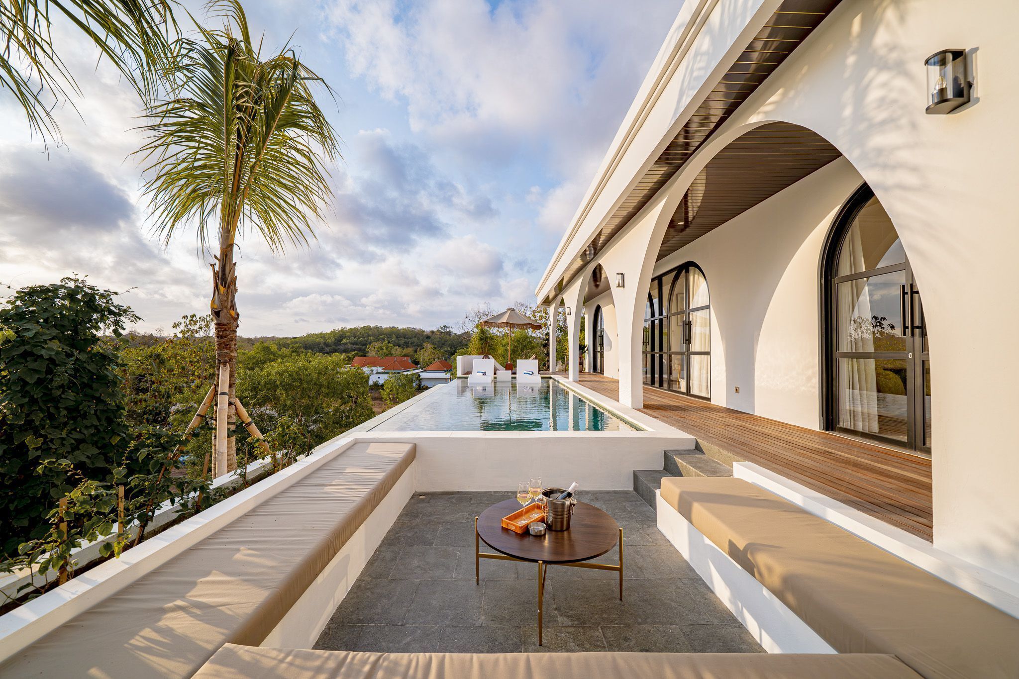 A poolside area with a table set for two, a palm tree, and a view of a distant landscape.