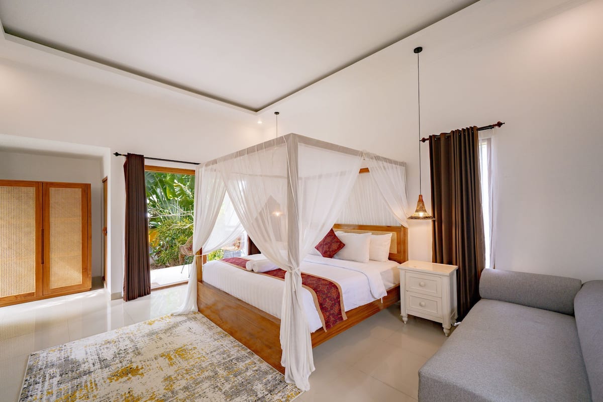 Een slaapkamer met een hemelbed, nachtkastje, lamp en een bank.