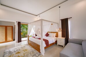 A bedroom with a four-poster bed, a bedside table, a lamp, and a sofa. - Jing Jang Villa Ungasan (Kutuh)