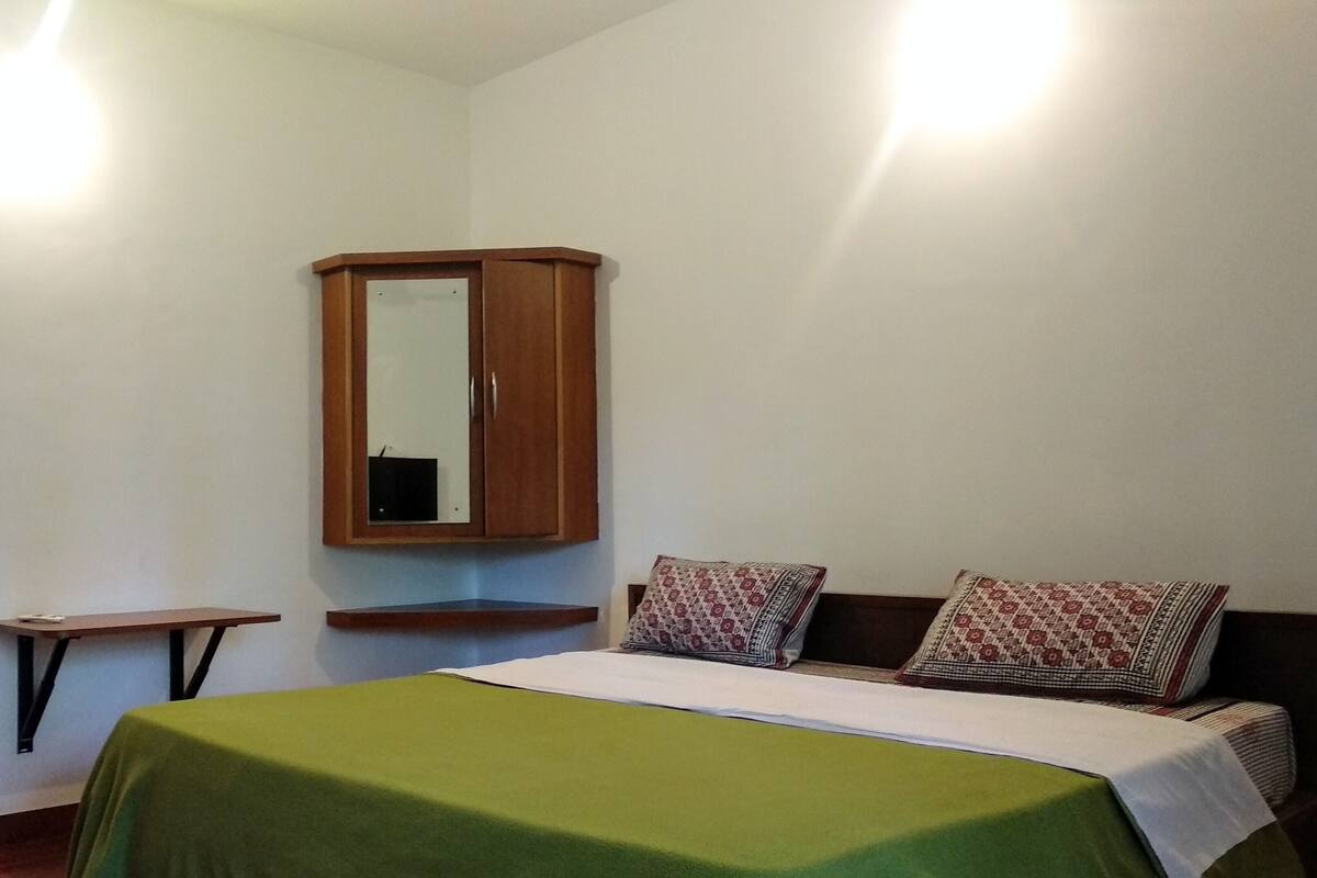 A bedroom with a bed, a bedside table, a mirror, and patterned pillows.