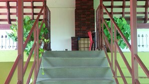 Eine Treppe mit roter Geländer führt zu einem überdachten Bereich mit Backsteinwand und grüner Wand.