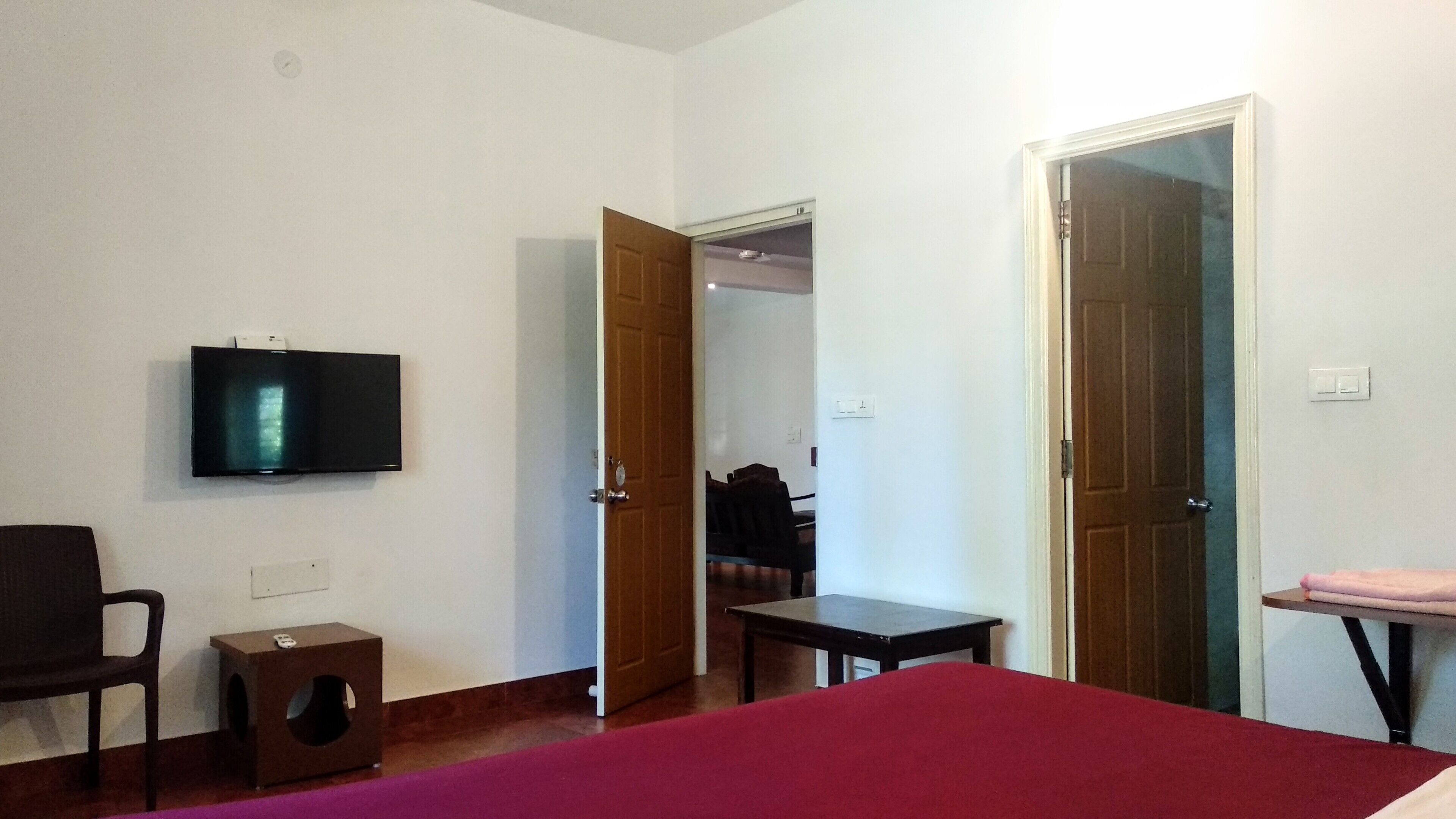 Una habitación con una cama, televisión, una mesita y dos puertas abiertas que dan a otras zonas.