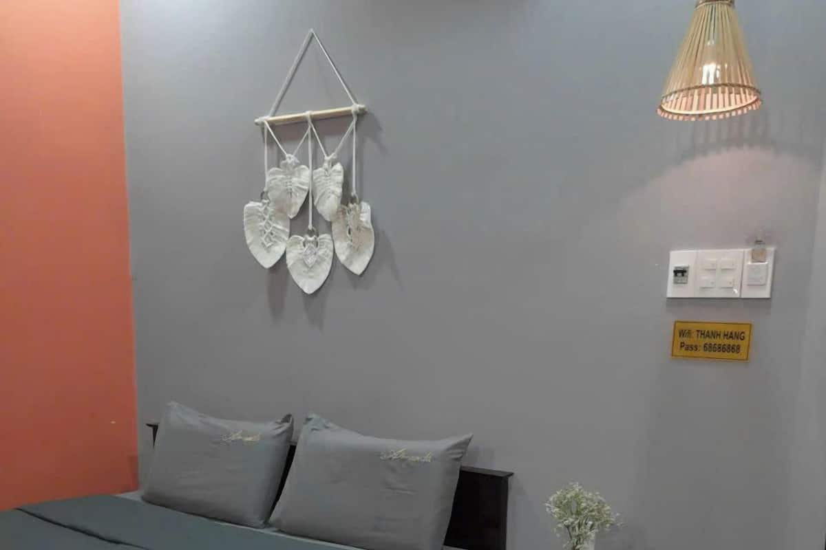 Une chambre à coucher comprenant un lit, une table de chevet avec un vase, un luminaire suspendu et une prise de courant fixée au mur.